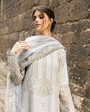 Woman wearing grey embroidered raw silk suit with diagonal color-blocked border under stone archway