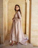 Side view of rose beige raw silk suit with organza dupatta draped over arm in stone corridor