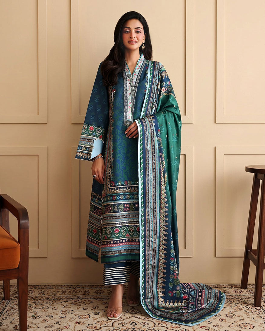 Woman wearing blue printed raw silk suit standing against a panelled wall with green dupatta