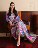 Woman wearing purple printed raw silk suit seated, showing striped hem border and dupatta