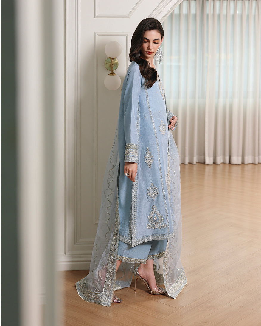 Side view of blue Korean raw silk shirt with embroidered hem, straight trouser and organza dupatta trailing