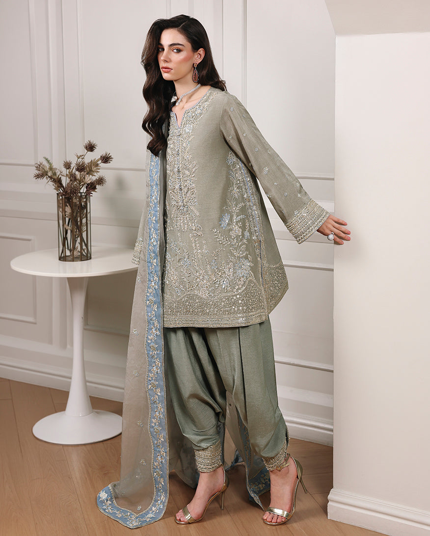 Side view of gray green Korean raw silk short shirt with embroidered hem, shalwar and organza dupatta
